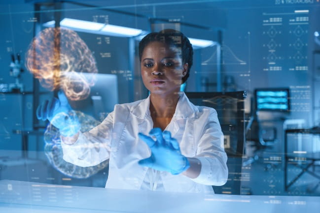 Young African-American doctor in a lab with a dark illumination in a lab coat and protective gloves works late with a HUD screen with a brain projection in a futuristic laboratory, we see her sitting at a table.