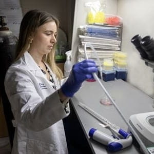 A woman in a white lab coat handles instruments in a science lab.