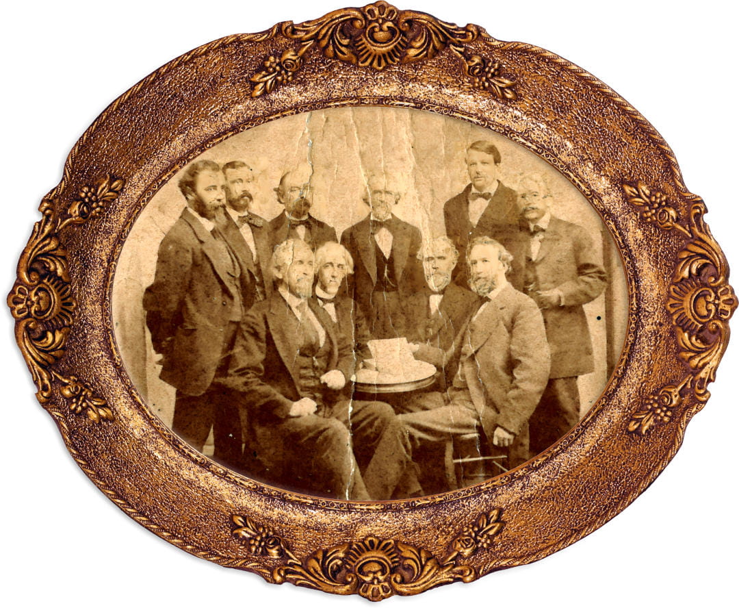 Ten men look at the camera, surrounding a table. The photo is wrinkled and in a circular frame.