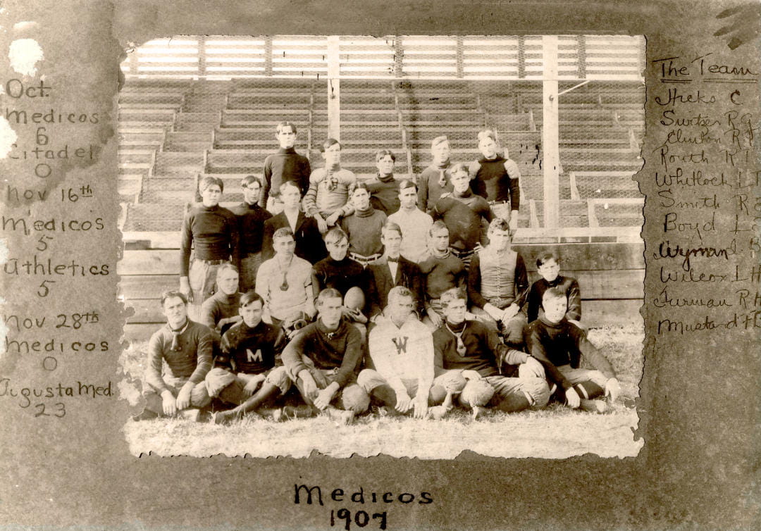 24 football players pose for a team photo in front of bleachers. The team’s scores and roster are handwritten around the photo.